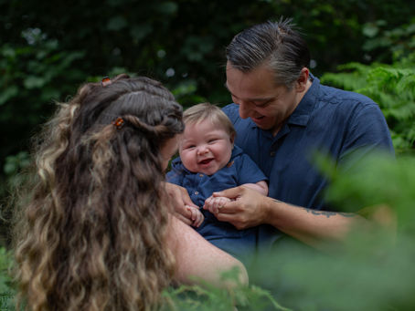 parents cradling a laughing baby boy in the woods