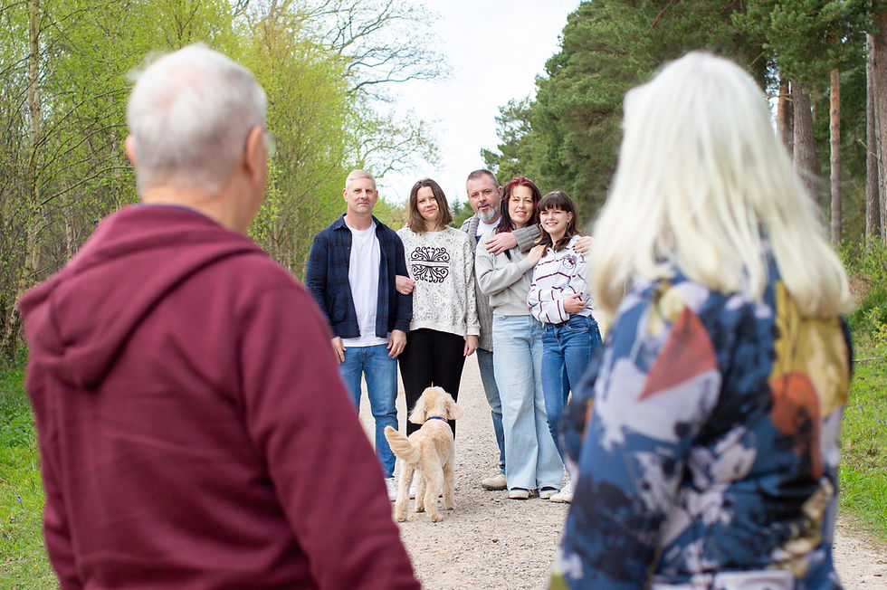 Blurred older couple faces a smiling family of five and a small dog on a tree-lined path.