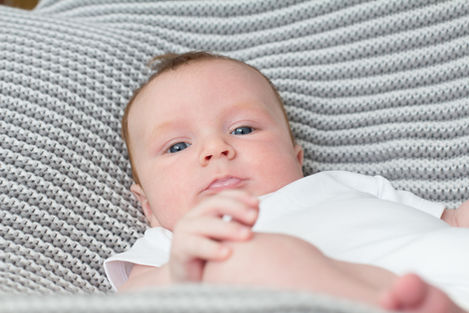 a baby with blue eyes is laying on a grey blanket