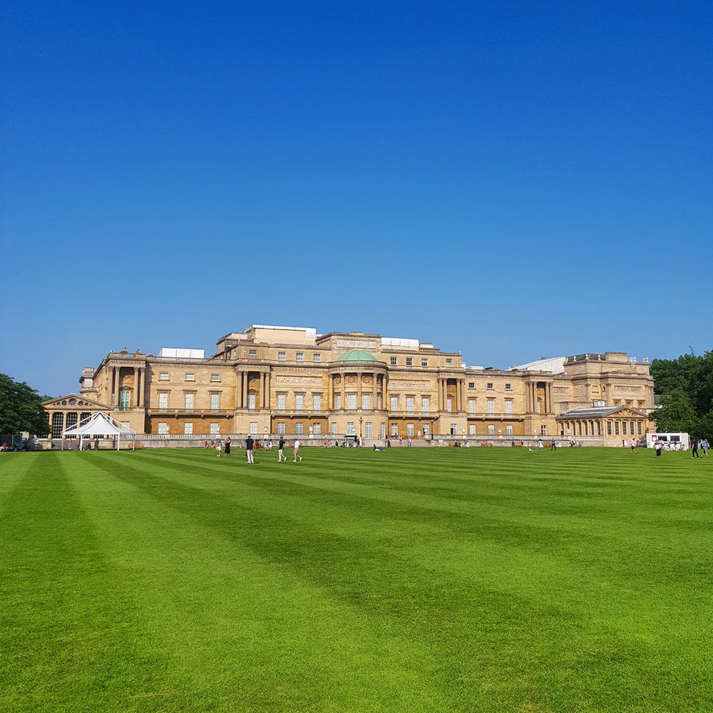 The garden front of Buckingham Palace across a freshly striped lawn under a clear blue sky