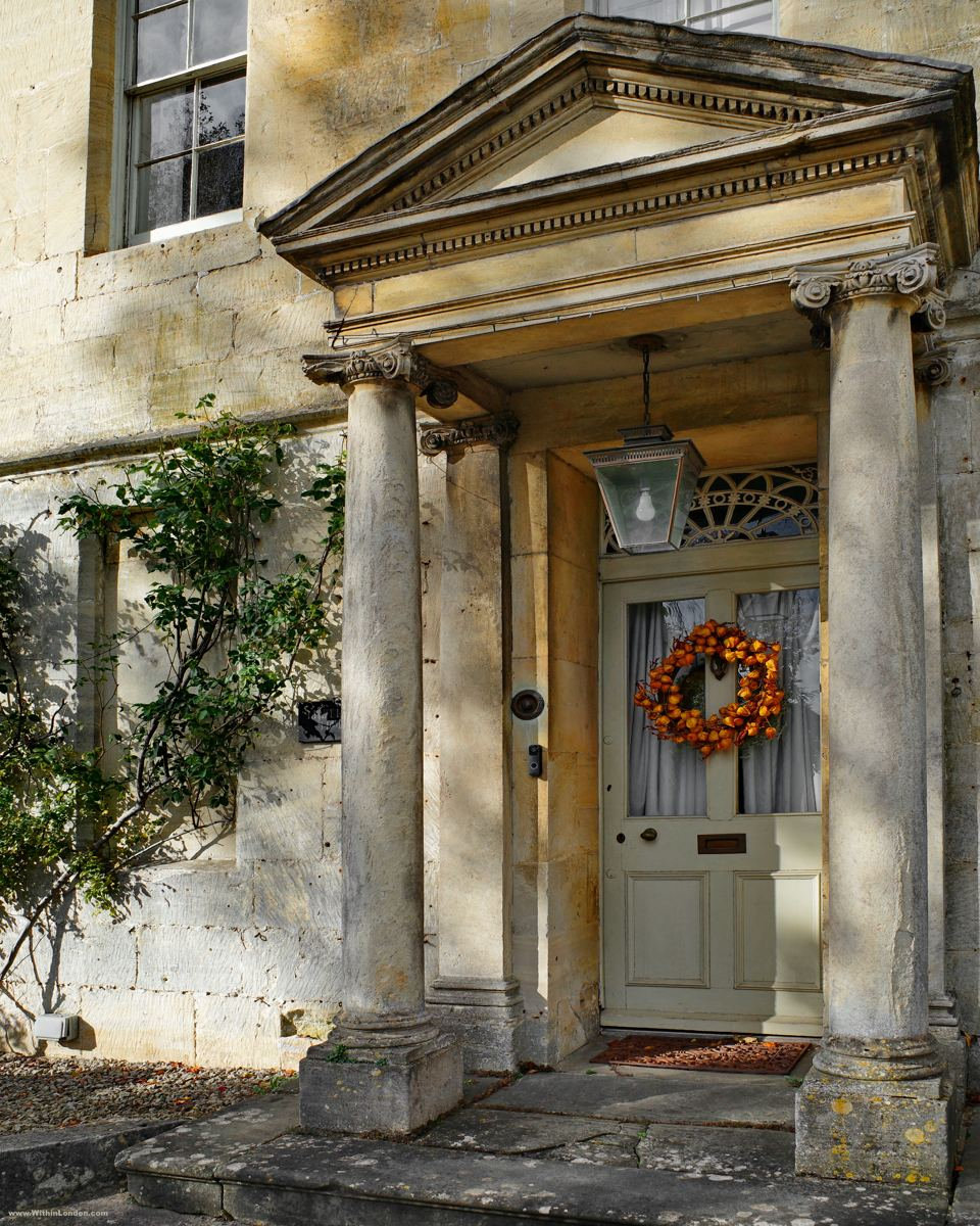 Classical doorway with a pediment on two stone columns, a hanging lantern and an orange leaf wreath on the door