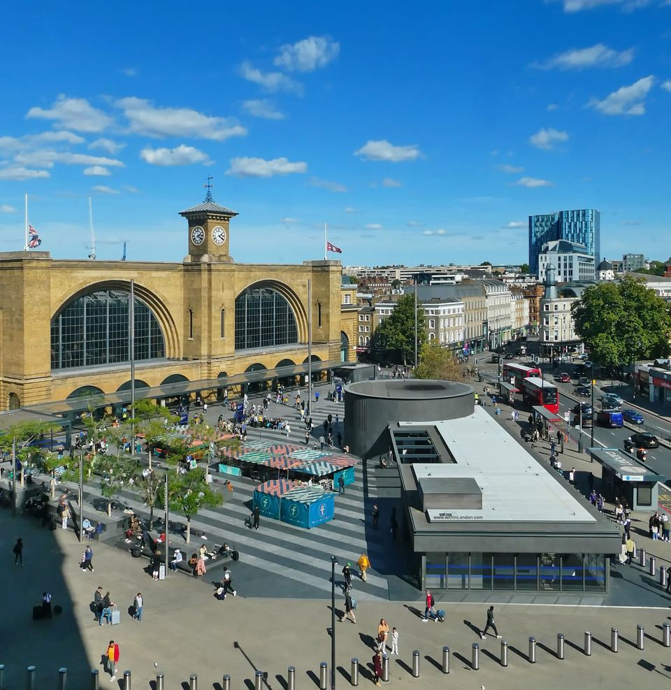 View from high above Euston Road over King's Cross station's twin arched windows and clock tower and the busy square in front