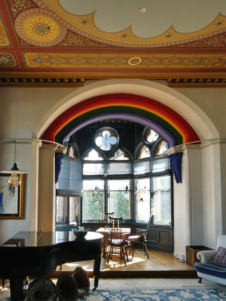 Close view of the painted rainbow arch over a Gothic bay window with round tracery, a small table and chairs set in the bay