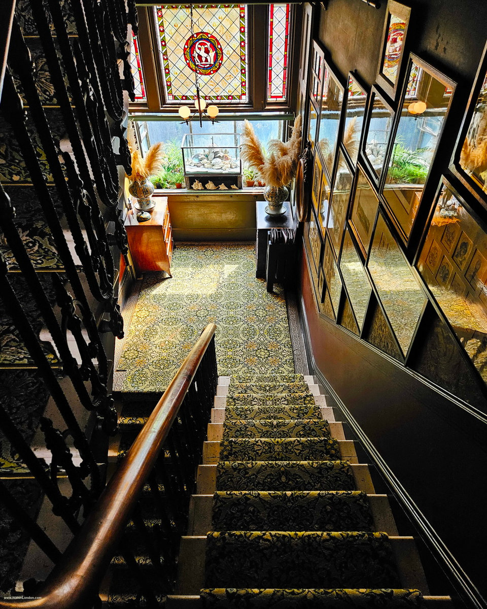 Looking down a Victorian staircase whose walls are hung with framed pictures up to the ceiling