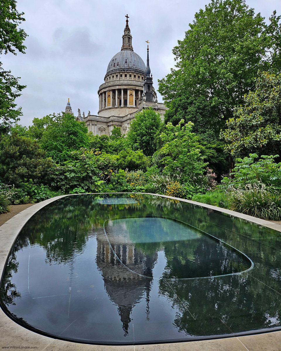 A dark oval pool in the Reflection Garden at 25 Cannon Street, mirroring the dome of St Paul's