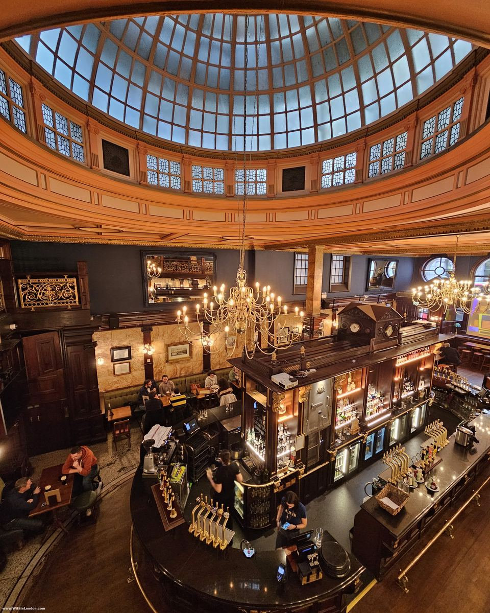 Orange coffered ceiling ring around a glass dome, above a busy oval bar and a full lunchtime floor