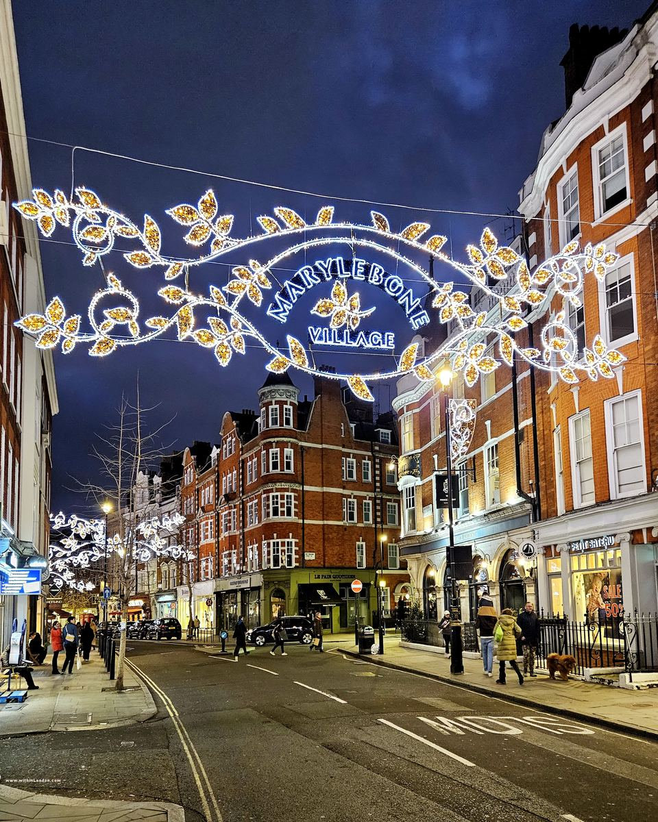 The lit Marylebone Village sign and garlands of gold leaves stretched across the high street at night