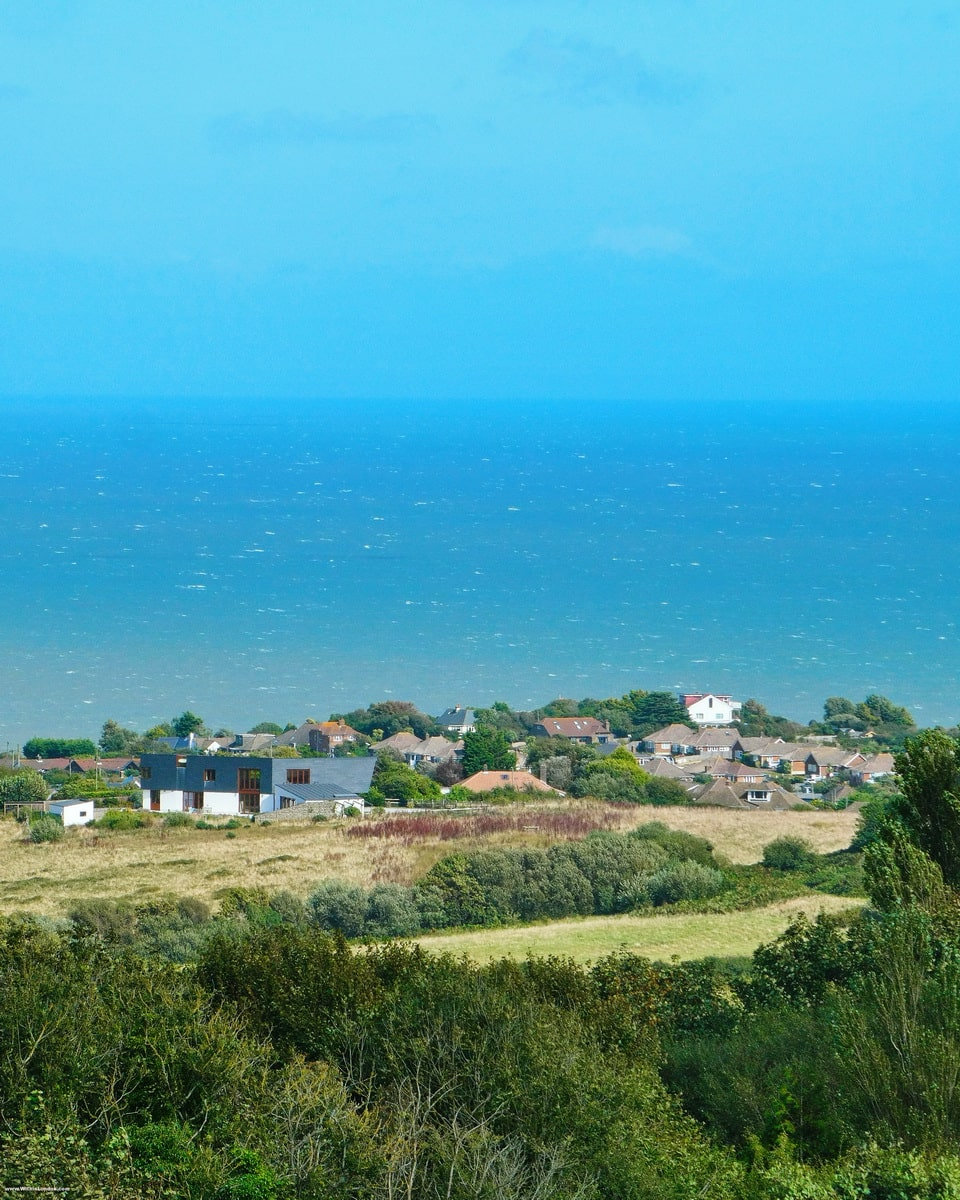 Green slopes of Hastings Country Park running down past houses to a bright blue sea