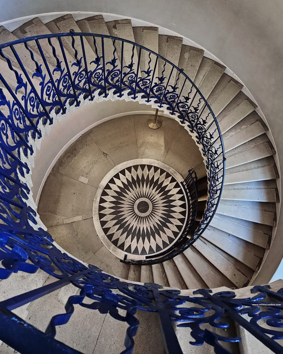 Looking down a stone spiral staircase with a flower-patterned blue wrought-iron balustrade