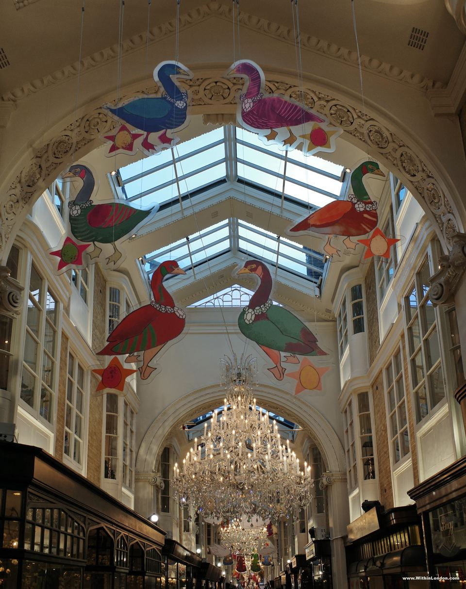 Painted long-necked birds hanging beneath the glazed roof of Burlington Arcade, with a crystal chandelier below them