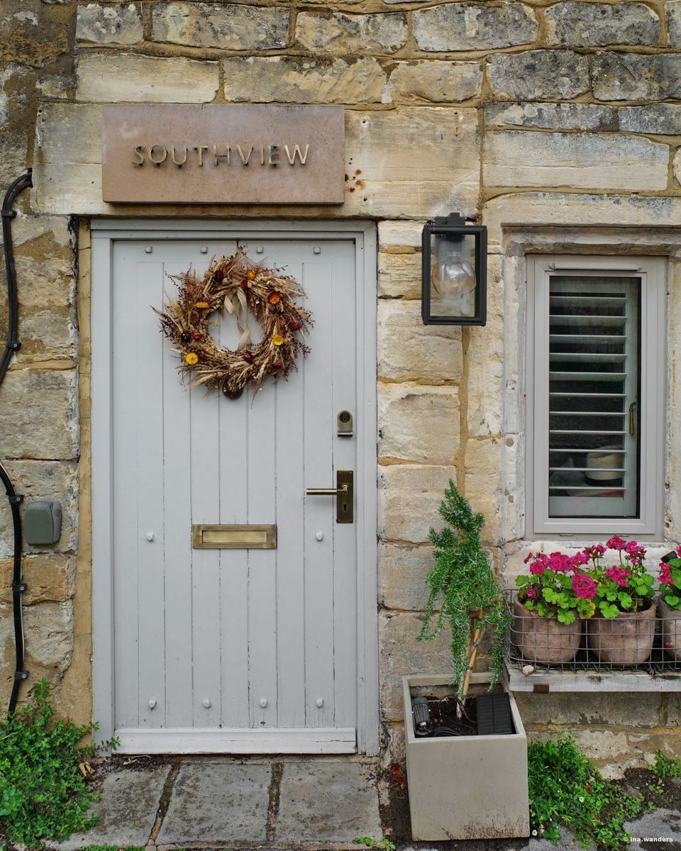 Pale grey door under a stone board reading Southview, with a dried-leaf wreath and a window box of pink geraniums