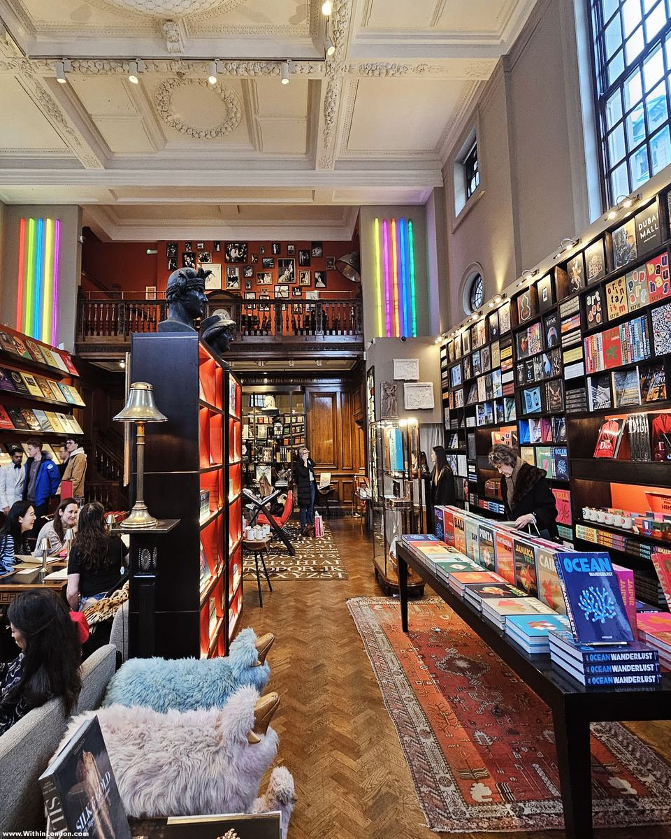 Long view of walls lined with books, a table of large coffee-table books, sheepskin-covered chairs and Persian rugs on a parquet floor