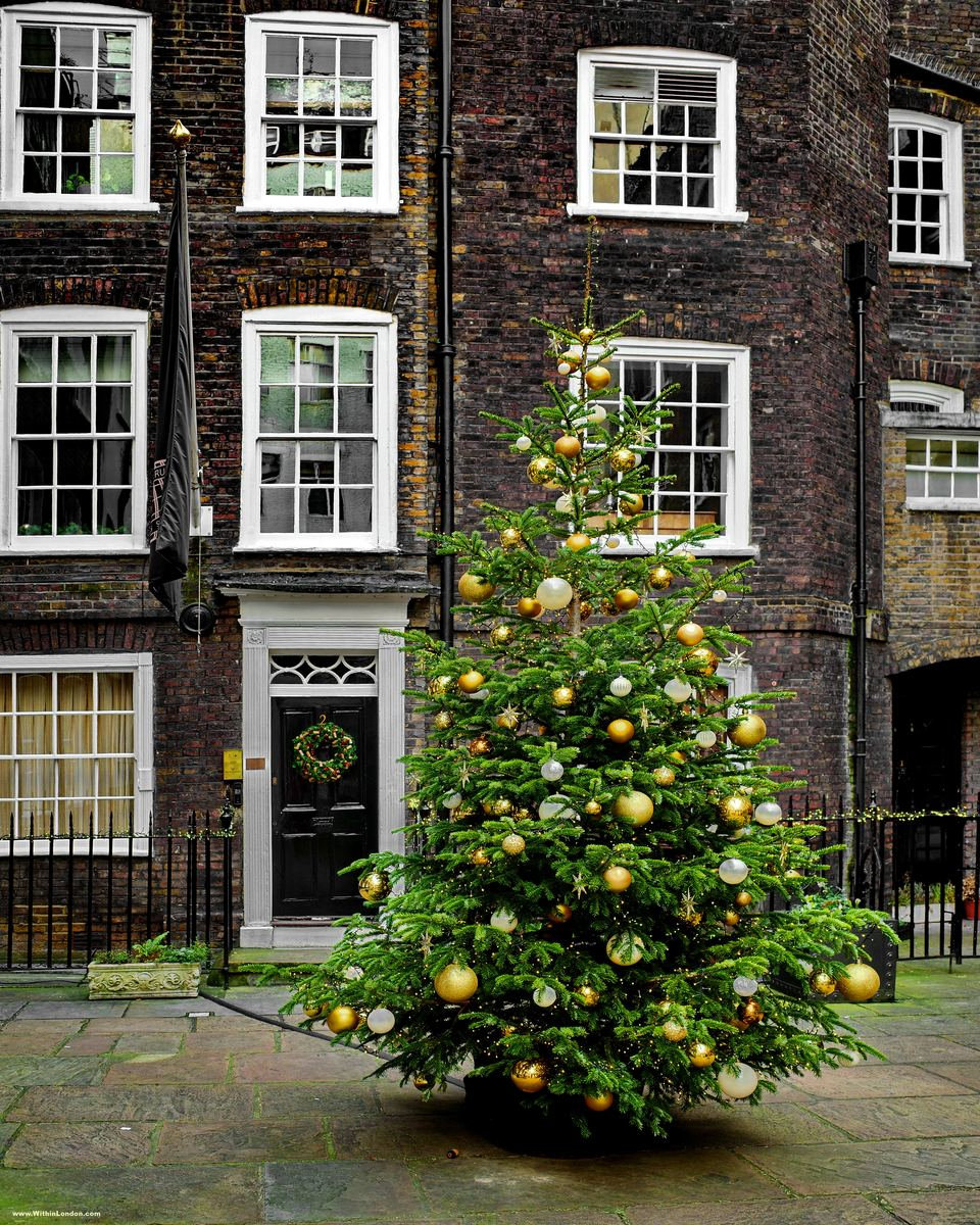 A Christmas tree with gold baubles in the middle of Pickering Place, in front of a dark-brick Georgian house with lanterns beside the door