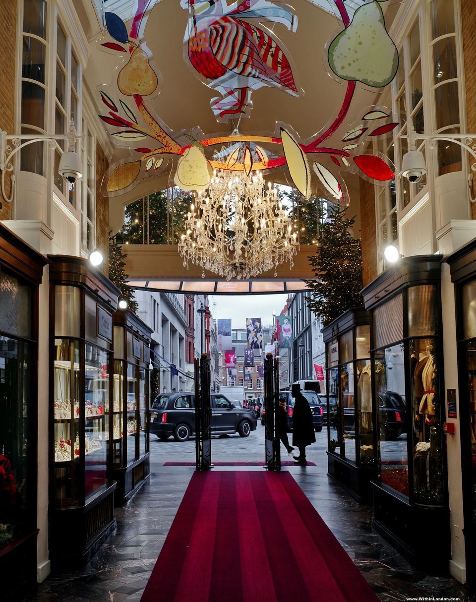 Looking out through the arcade entrance along a red carpet to the street, with hanging painted pears and leaves and a chandelier overhead