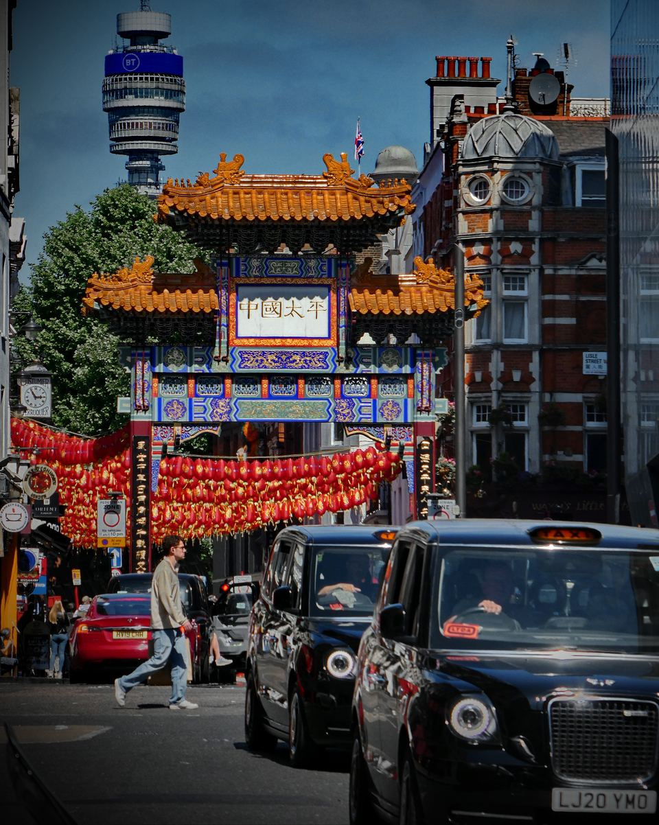 The large Chinese paifang gate on Wardour Street in London's Chinatown, with red lanterns strung beyond it and the BT Tower behind