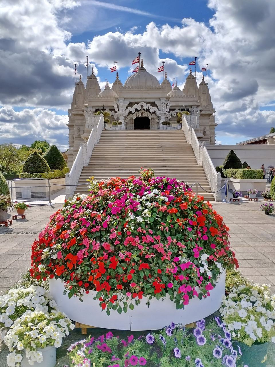 A large round white planter overflowing with red, pink and white flowers at the bottom of the steps leading up to the temple