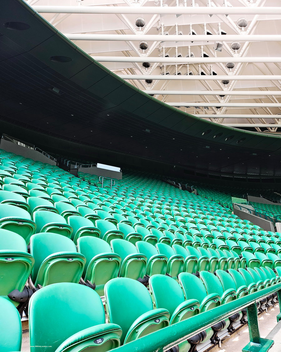 Rows of empty green seats curving round a court beneath white roof trusses