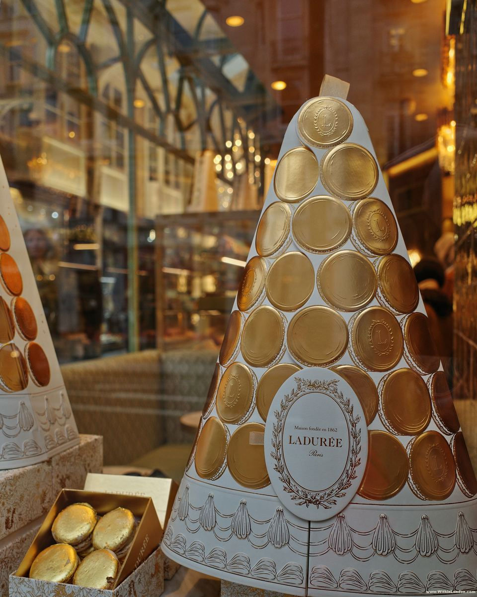 A cone of gold macaron discs in a Ladurée window, with a box of gold macarons beside it