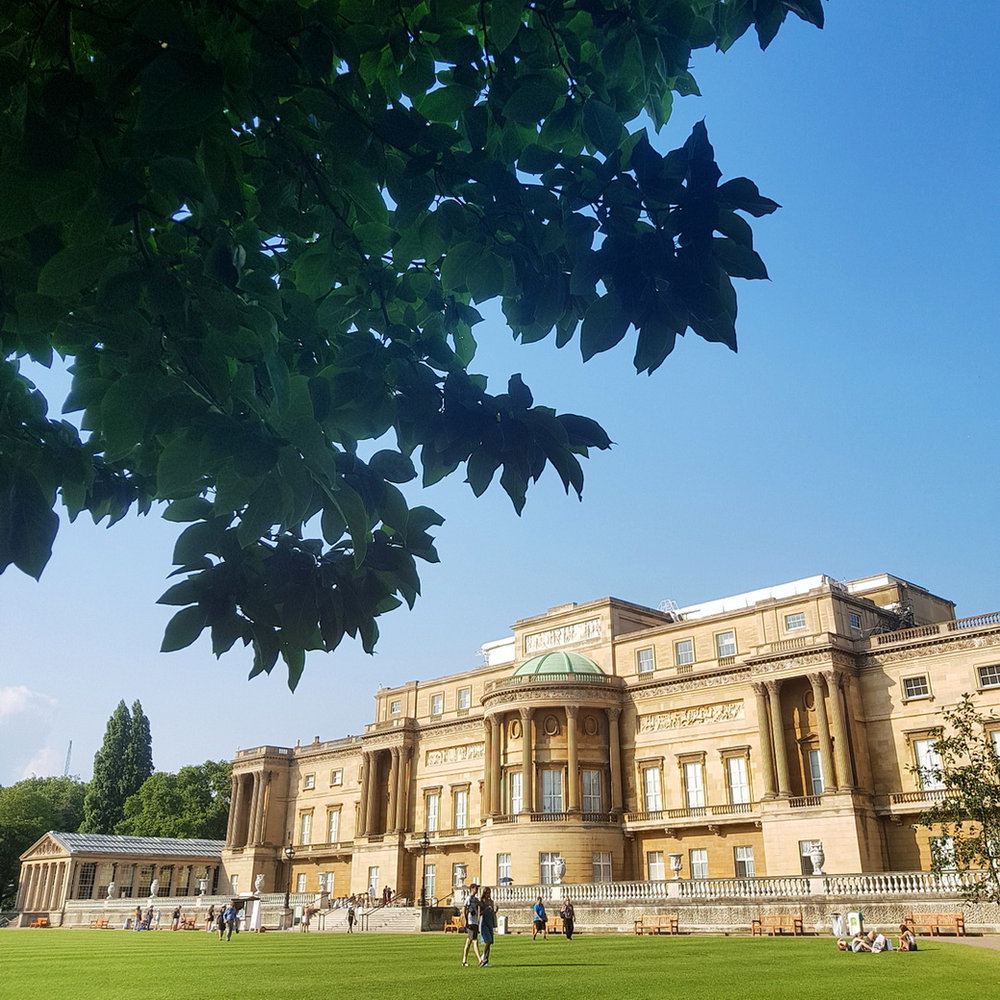 The garden front of Buckingham Palace seen beneath leafy branches against a deep blue sky