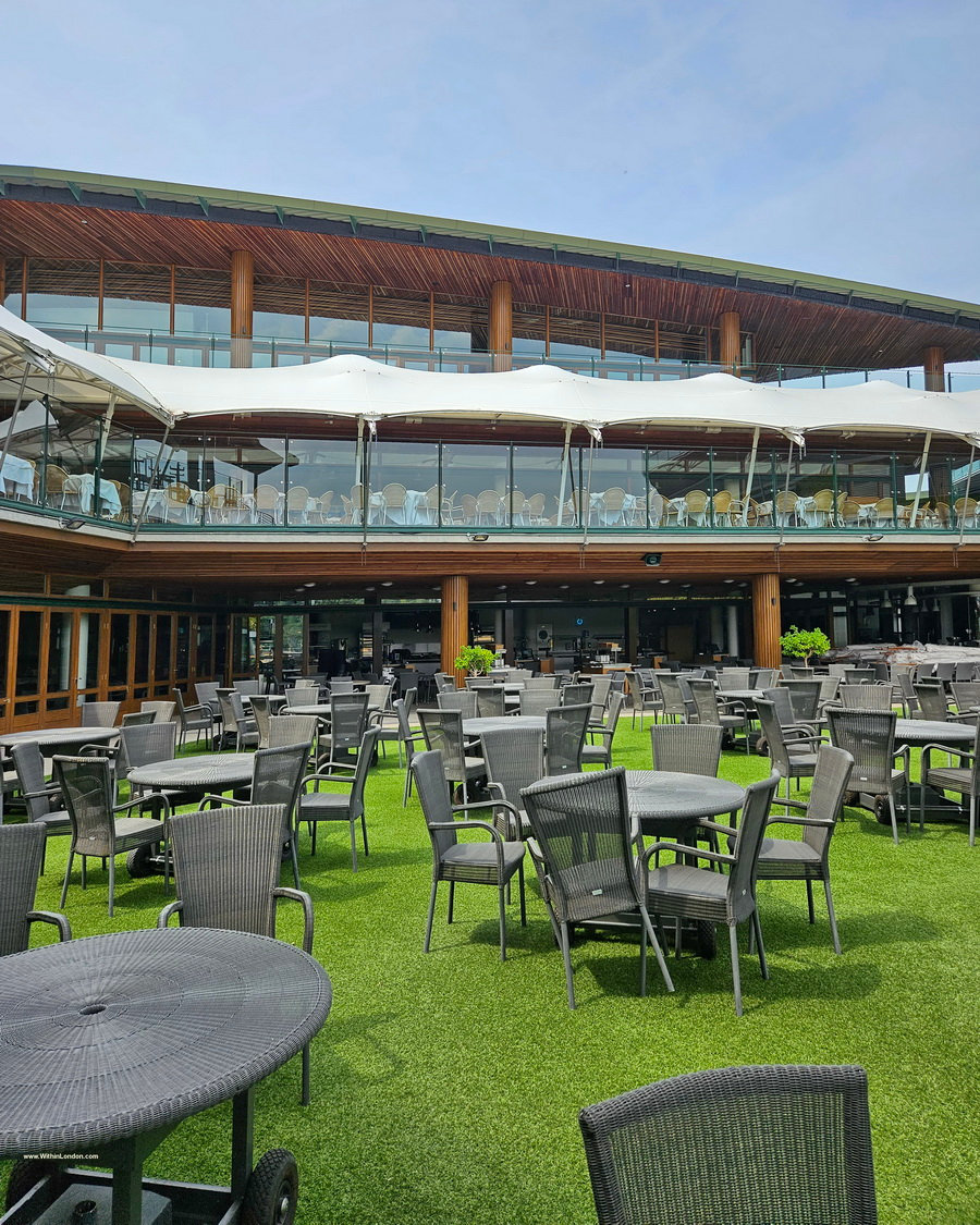 Empty terrace with grey chairs and round tables on artificial grass in front of a modern building with balconies