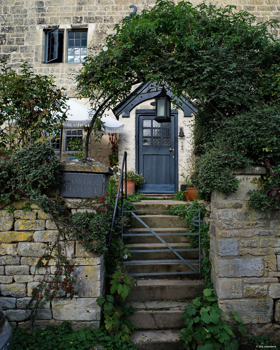 Steep stone steps rising to a dark blue door under a leafy arch with a lantern above