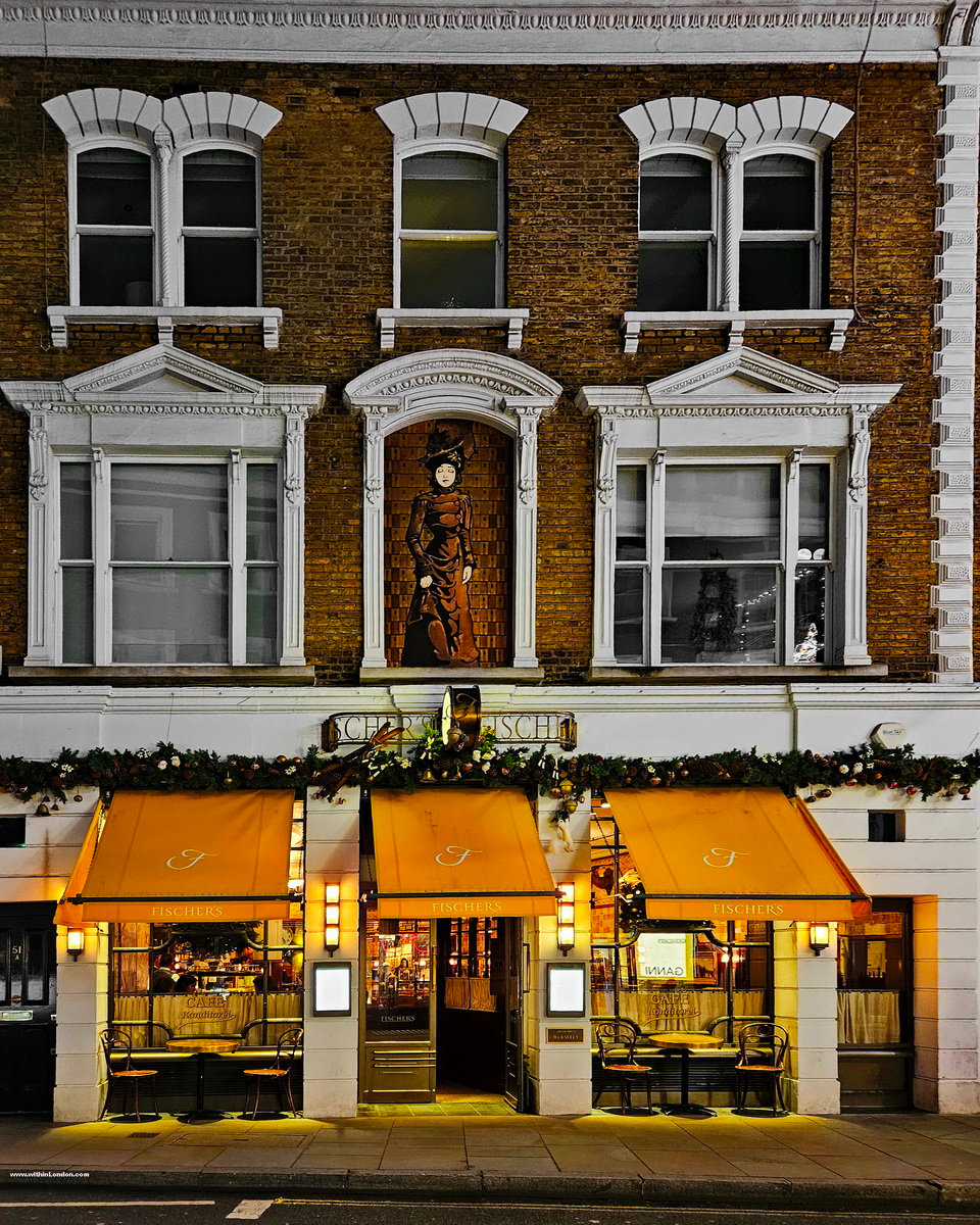 Brick building on Marylebone High Street with white window surrounds, lit windows under yellow awnings and a festive garland along the front