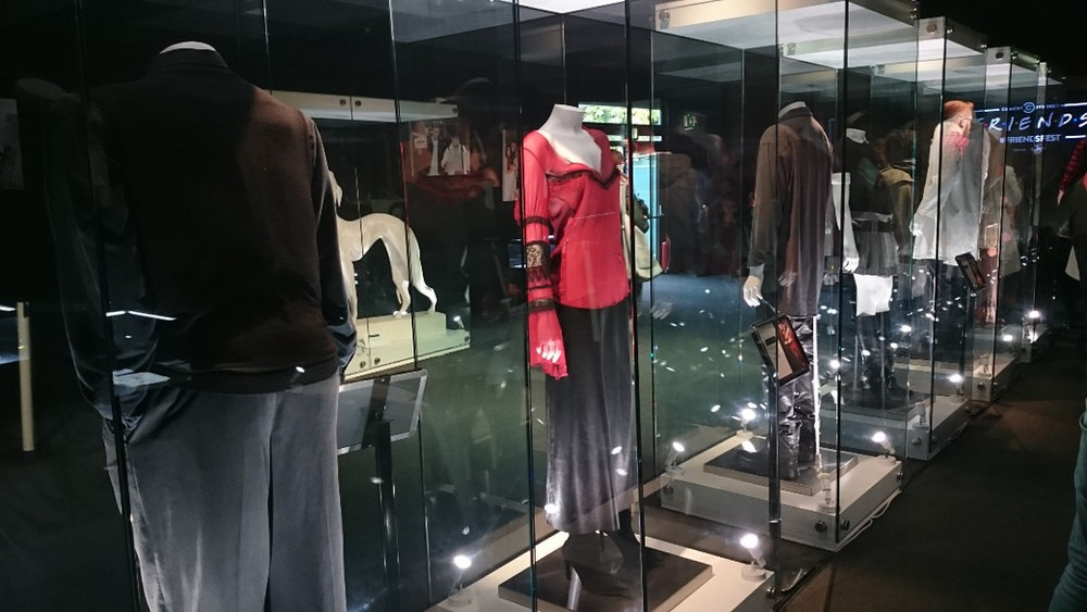 Mannequins in a glass case wearing costumes from the show, lit against a dark wall.