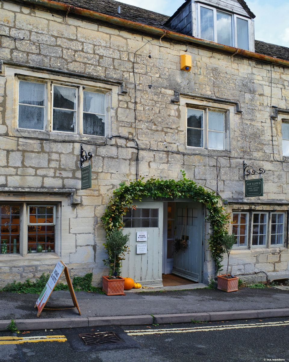 Stone-fronted building on a Painswick street with an ivy arch over its door and a sandwich board on the pavement