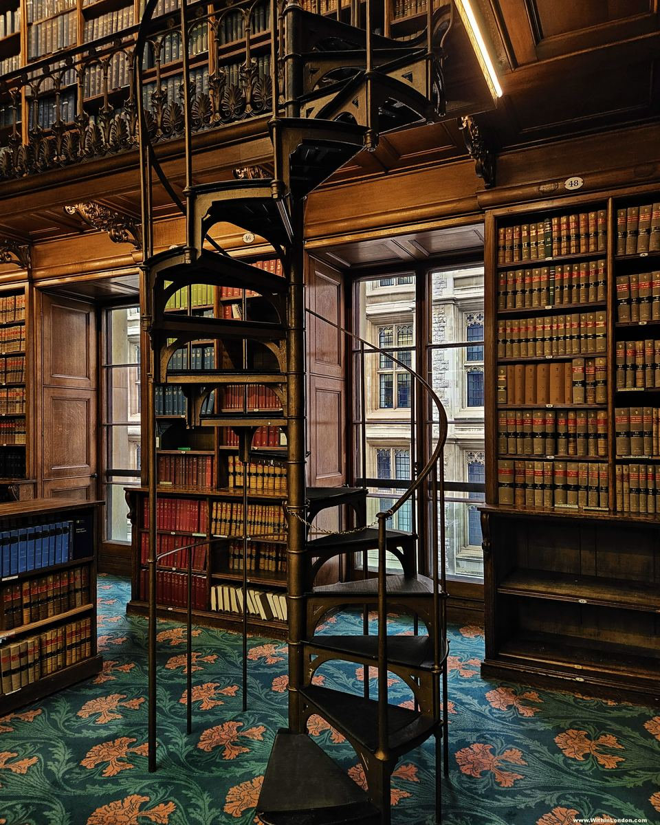 A black cast-iron spiral staircase in the corner of a law library, with Gothic stonework beyond