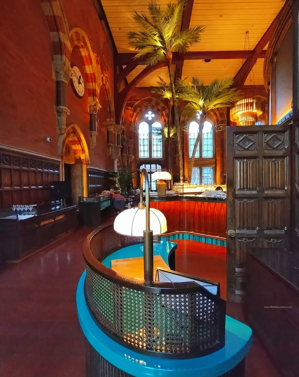 Turquoise and cane host stand with a globe lamp next to a carved dark wooden door and panelled walls