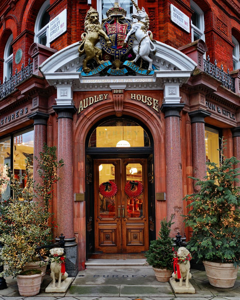 The red granite doorway of Purdey's Audley House on South Audley Street, with the royal coat of arms above and potted trees either side