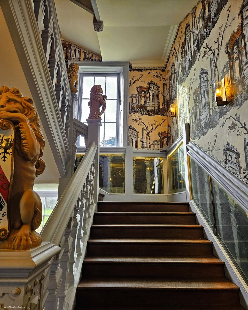 A Jacobean staircase with a carved lion on the newel post, against a sepia scenic wallpaper
