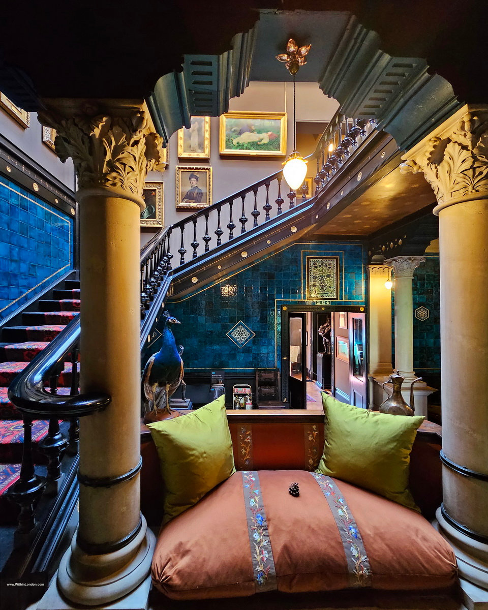 A stair hall lined with peacock-blue tiles, with a dark wooden staircase and a stuffed peacock