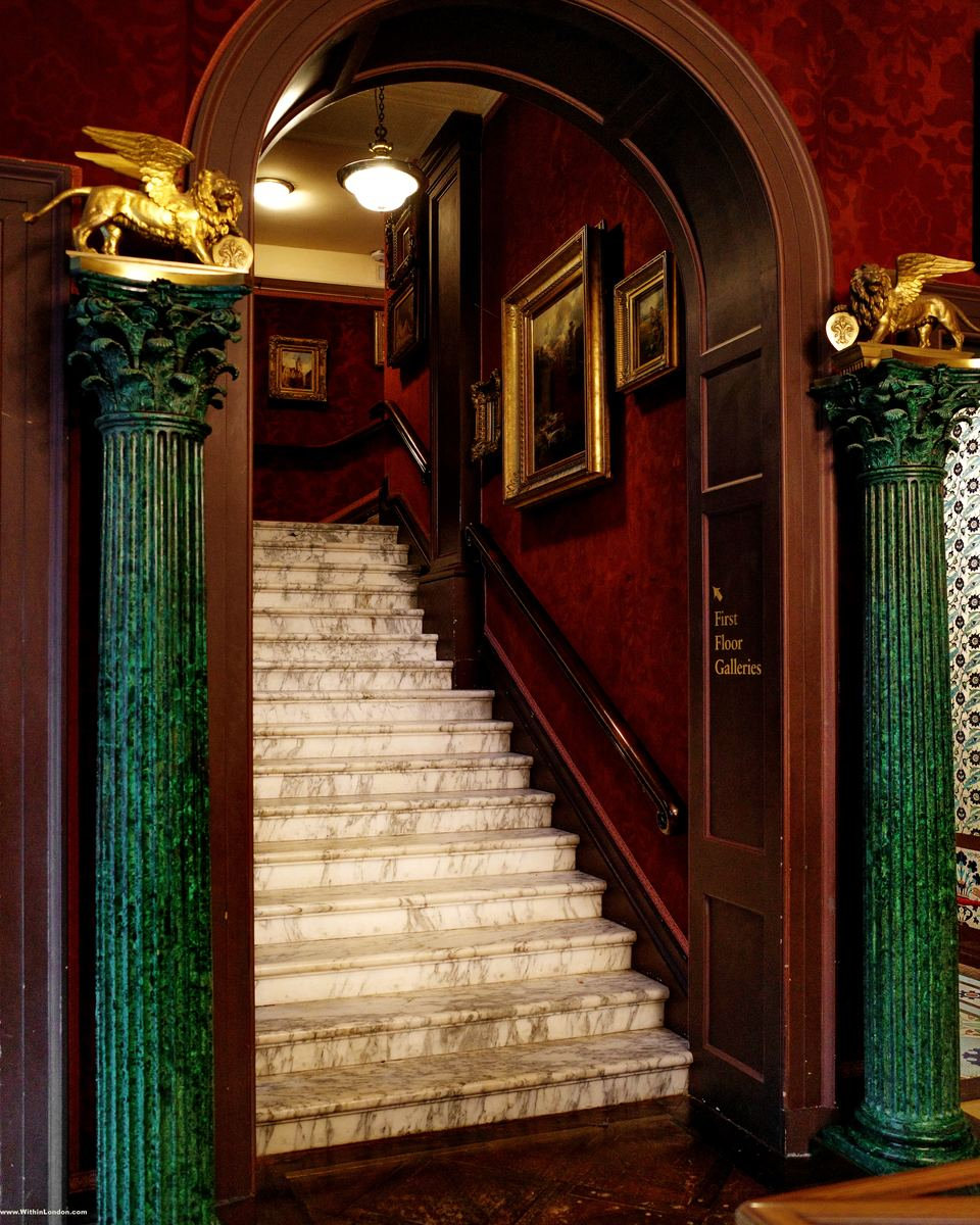 A grand staircase rising between green marbled columns topped with gilded winged lions