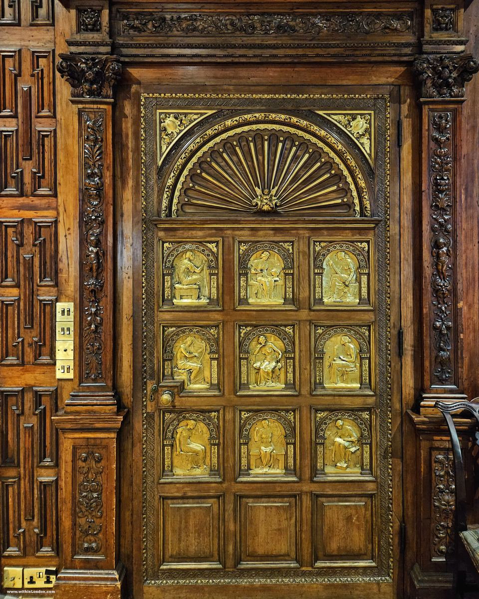 Carved wooden door with gilded relief panels of figures beneath a shell-shaped arch