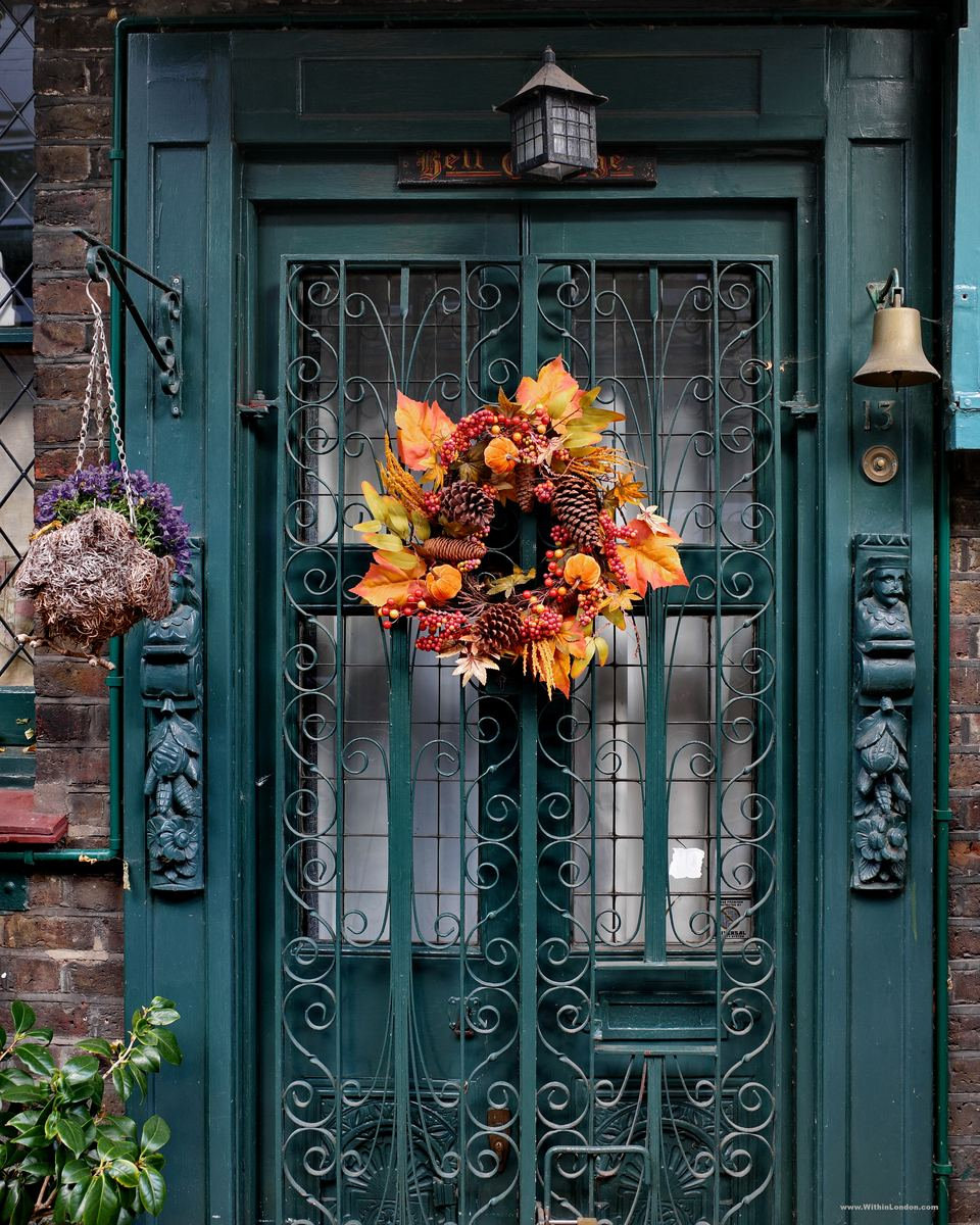 A teal front door with decorative ironwork and an autumn wreath of orange maple leaves hung in the centre