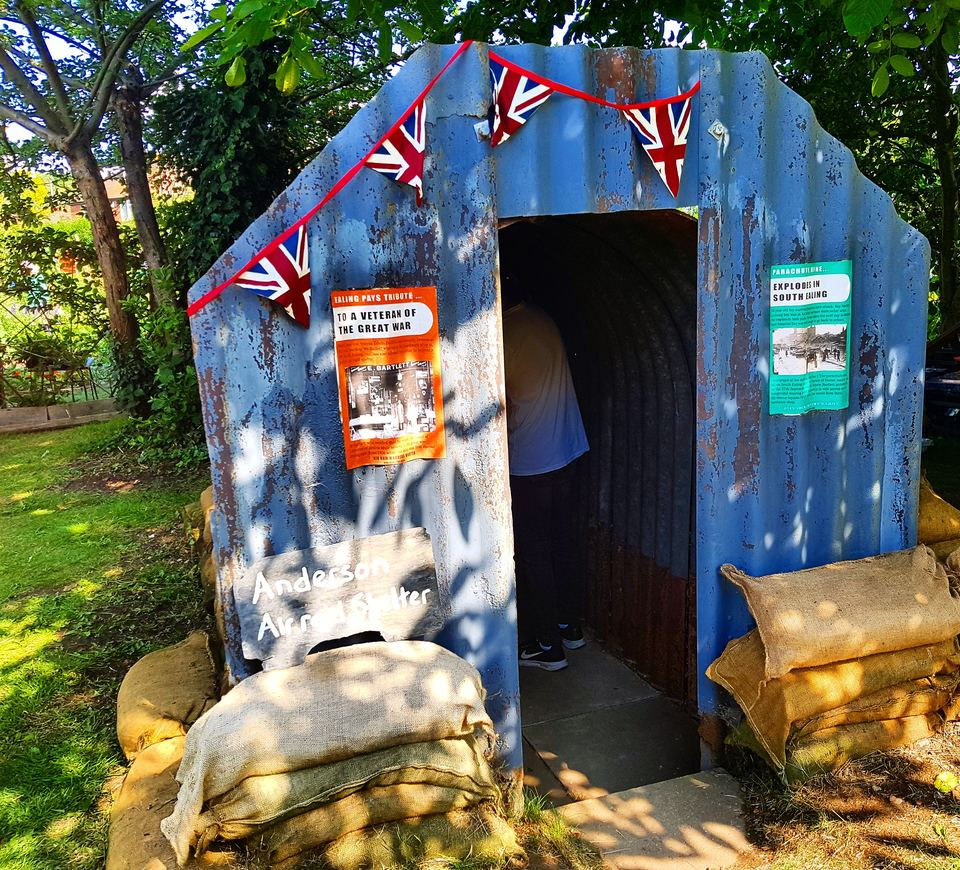 Restored corrugated iron Anderson shelter on the heritage plot at Northfields Allotments, hung with bunting and banked with sandbags