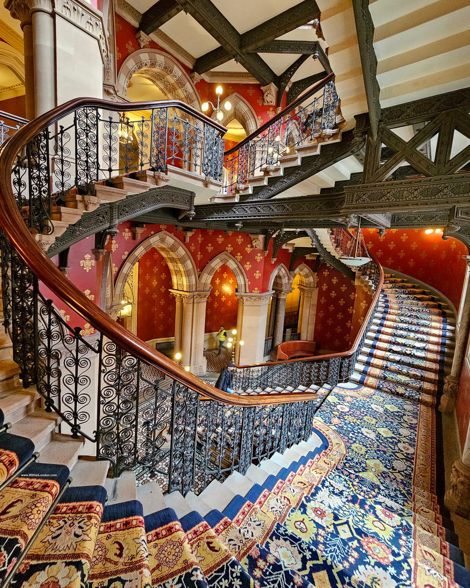 A marble staircase curving down past a gilded handrail and a dark cast-iron balustrade in a Gothic Revival hotel