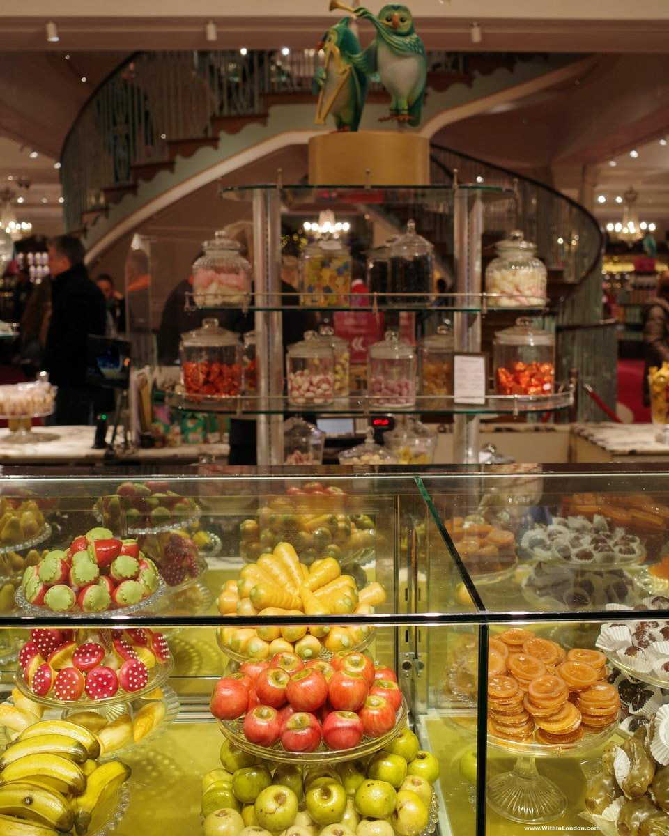 Jars of sweets on shelves above a glass counter piled with strawberries, bananas and apples, inside Fortnum & Mason