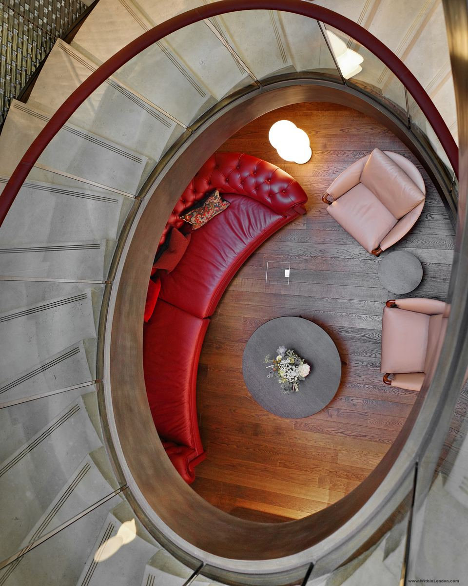Looking down an oval spiral staircase onto a curved red leather sofa