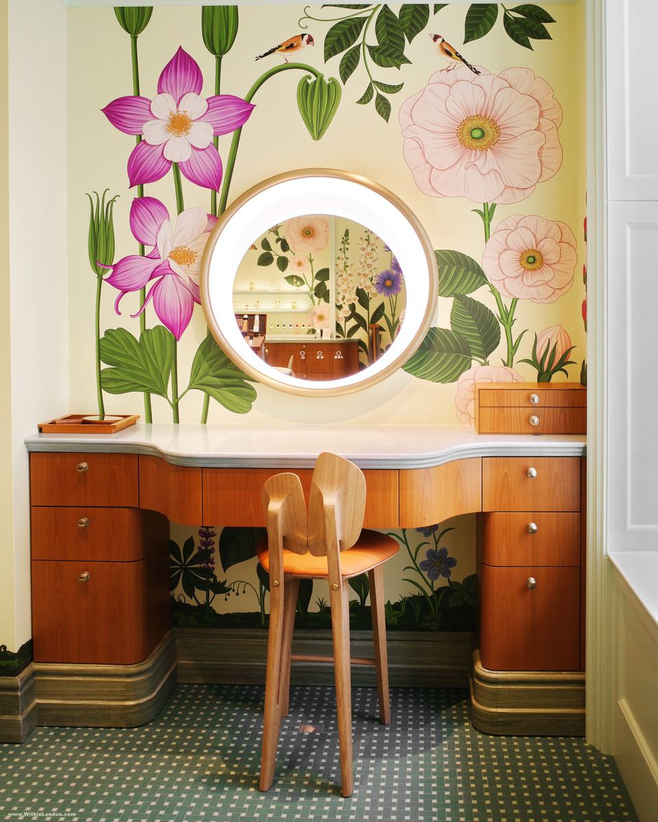 A cherrywood dressing table and round lit mirror in the beauty room at Hermès Bond Street, with Katie Scott's oversized botanical illustrations covering the walls