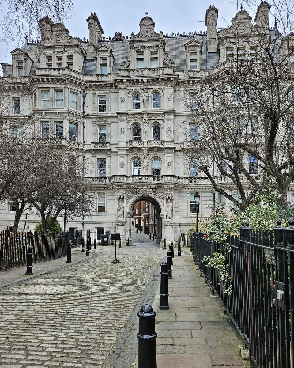 Cobbled lane lined with black bollards leading to a grand white stone building with an arched passage