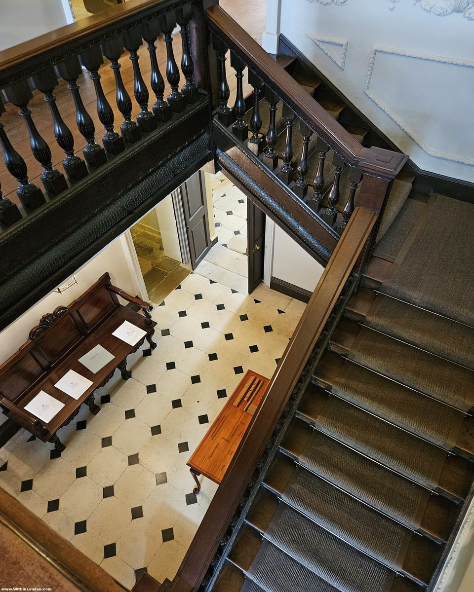 Looking down a mahogany staircase with twisted balusters to a black-and-white chequered stone floor