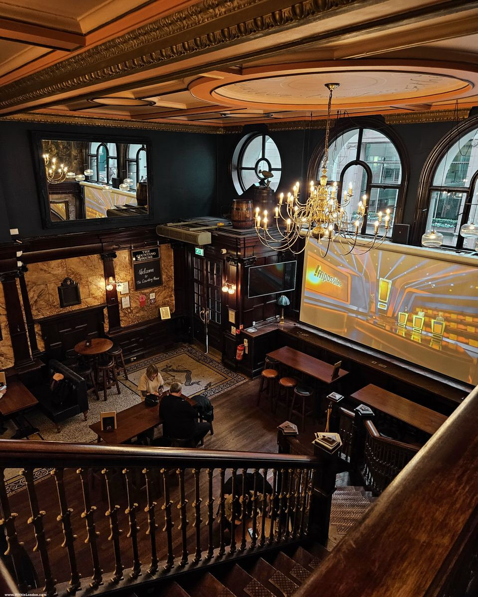 Wooden staircase rising to a gallery past dark blue walls, marble pillars, round and arched windows and a sports screen