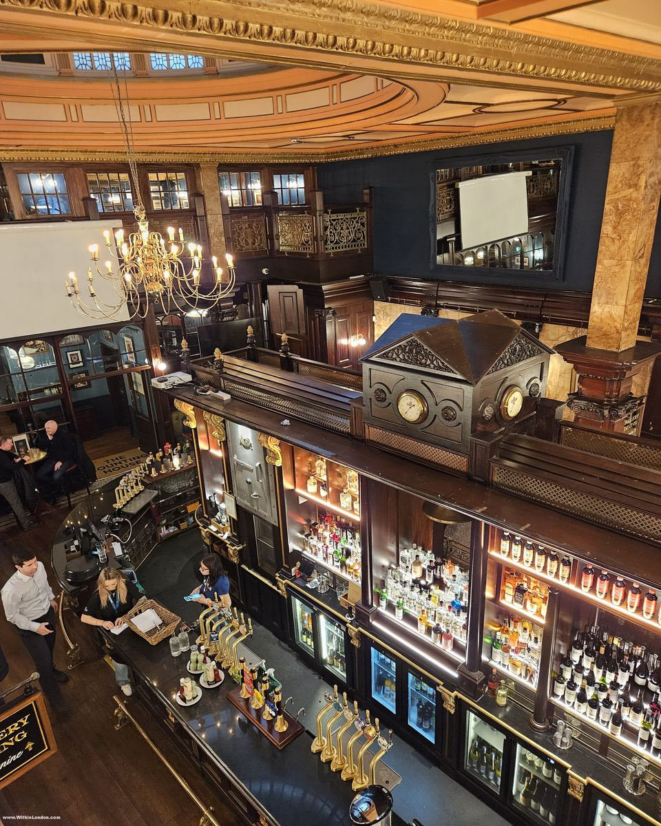 Bar staff working below lit bottle shelves and a clock-topped back-bar, with a Gallery Dining sign on the wall