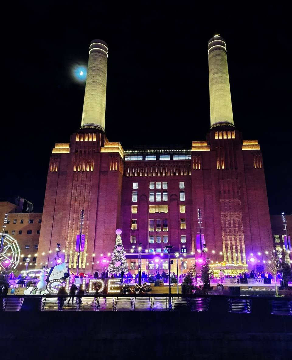 The floodlit brick front of Battersea Power Station and two white chimneys at night, with a lit GLIDE sign and the rink in front