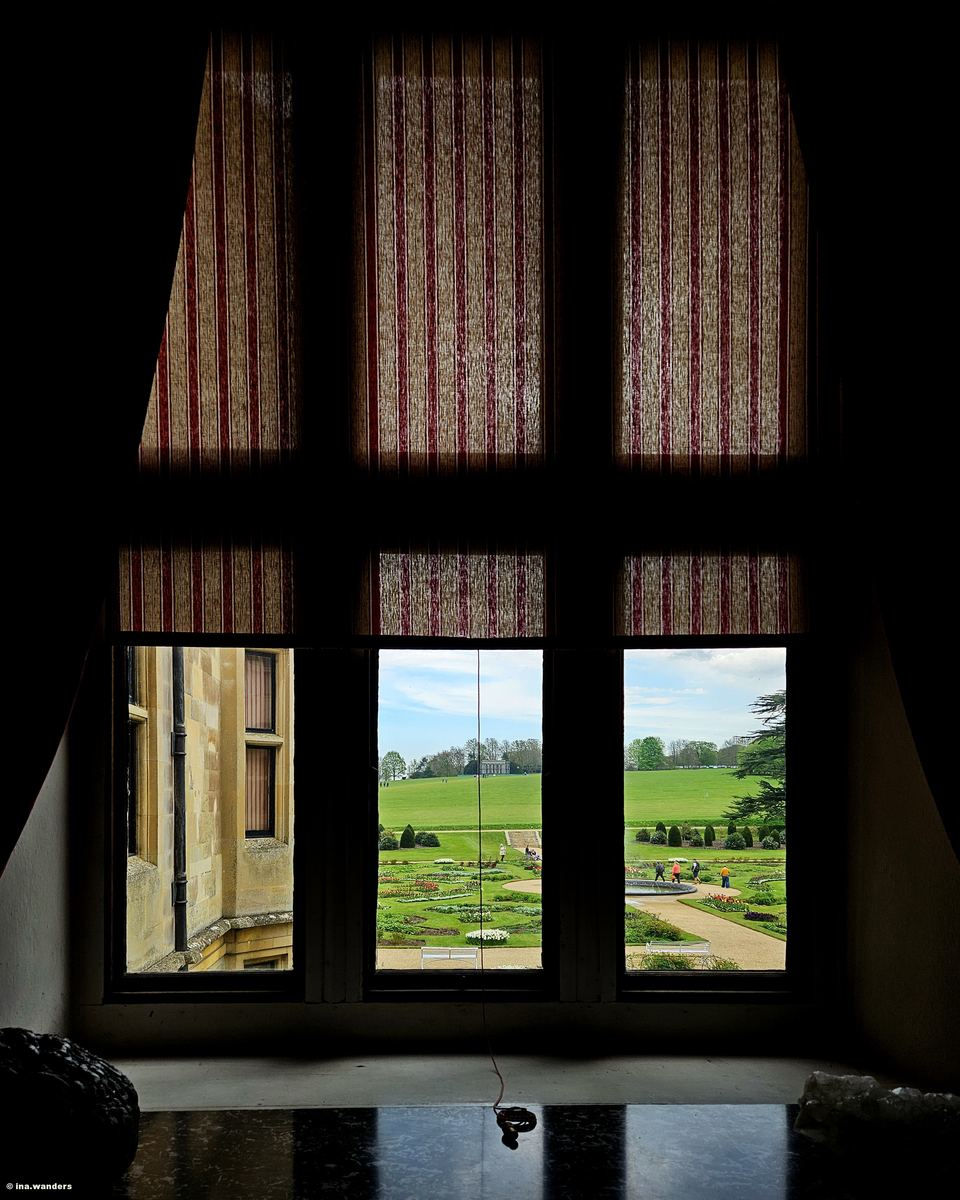 A dark panelled room at Audley End House with the shutters half closed and a mullioned window looking out over the parterre and parkland