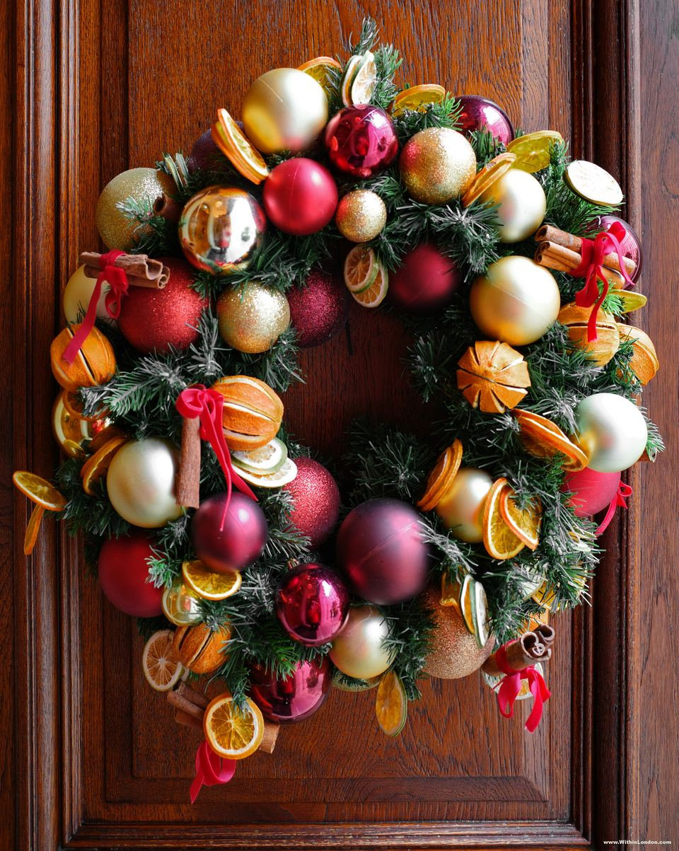 A wreath of red and gold baubles, dried orange slices and cinnamon sticks on a dark wooden door