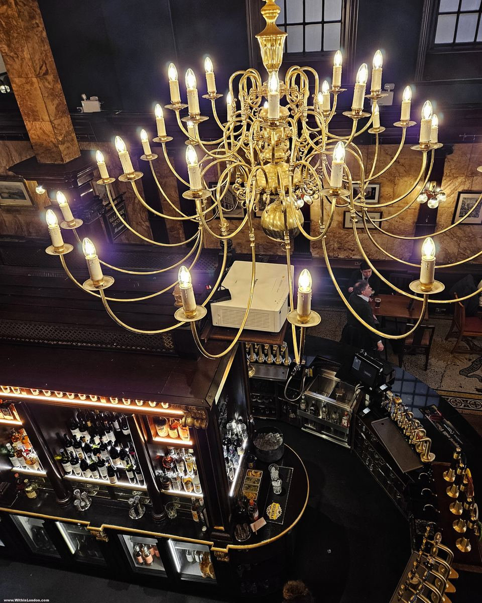 Close view of a many-armed brass chandelier with candle-shaped bulbs hanging over a pub bar
