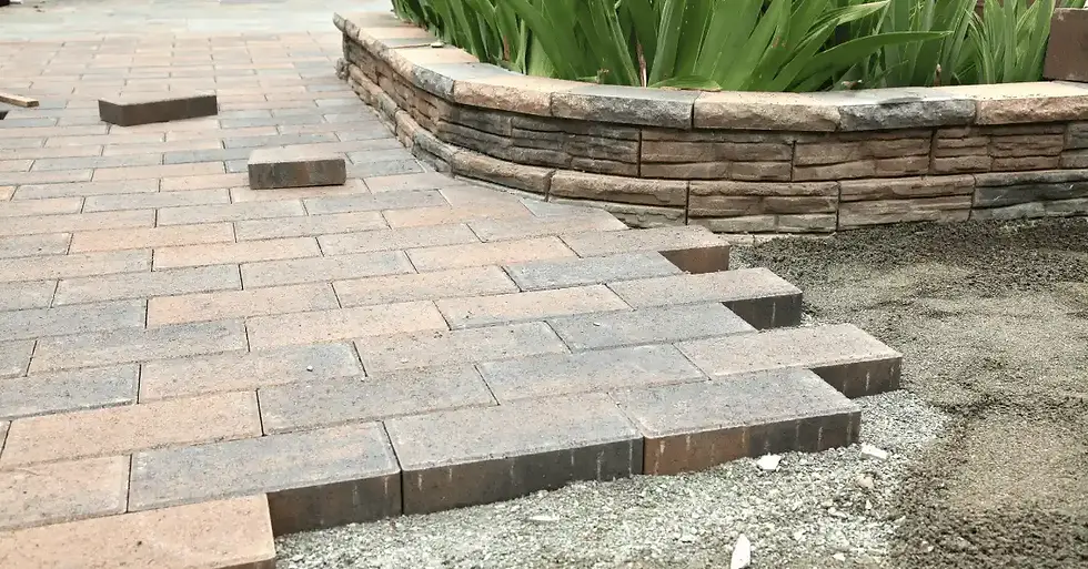 Paver patio installation in progress with interlocking concrete pavers and a curved raised garden wall.